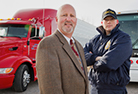 man in suit and a FMCSA state official standing in front of a red commercial motor vehicle